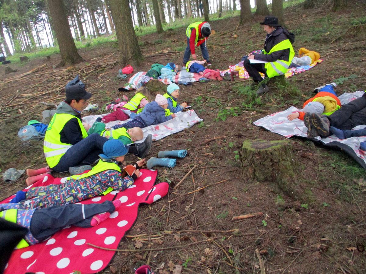 Eine Gruppe Kinder liegt auf Picknickdecken im Wald