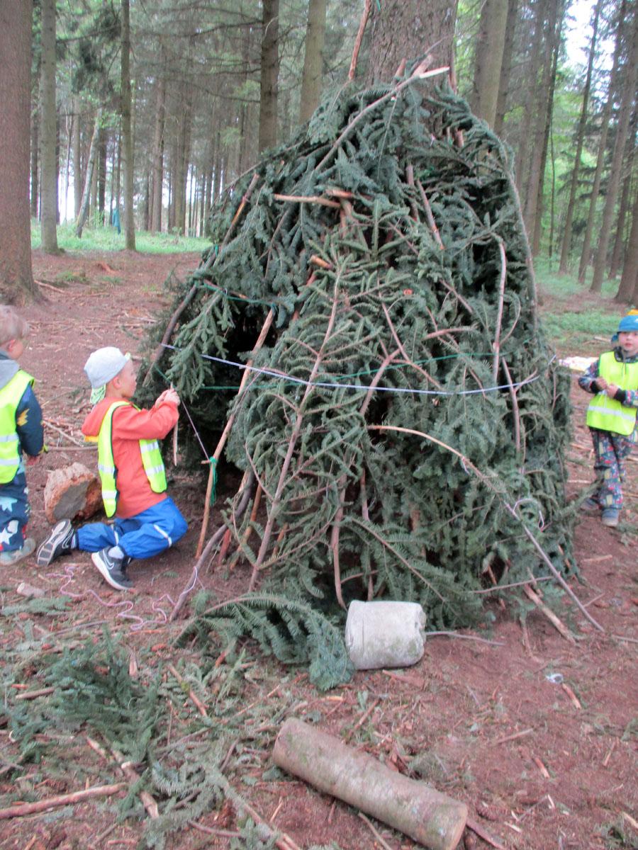 3 Kinder bauen an einem Tipi aus Waldmaterialien