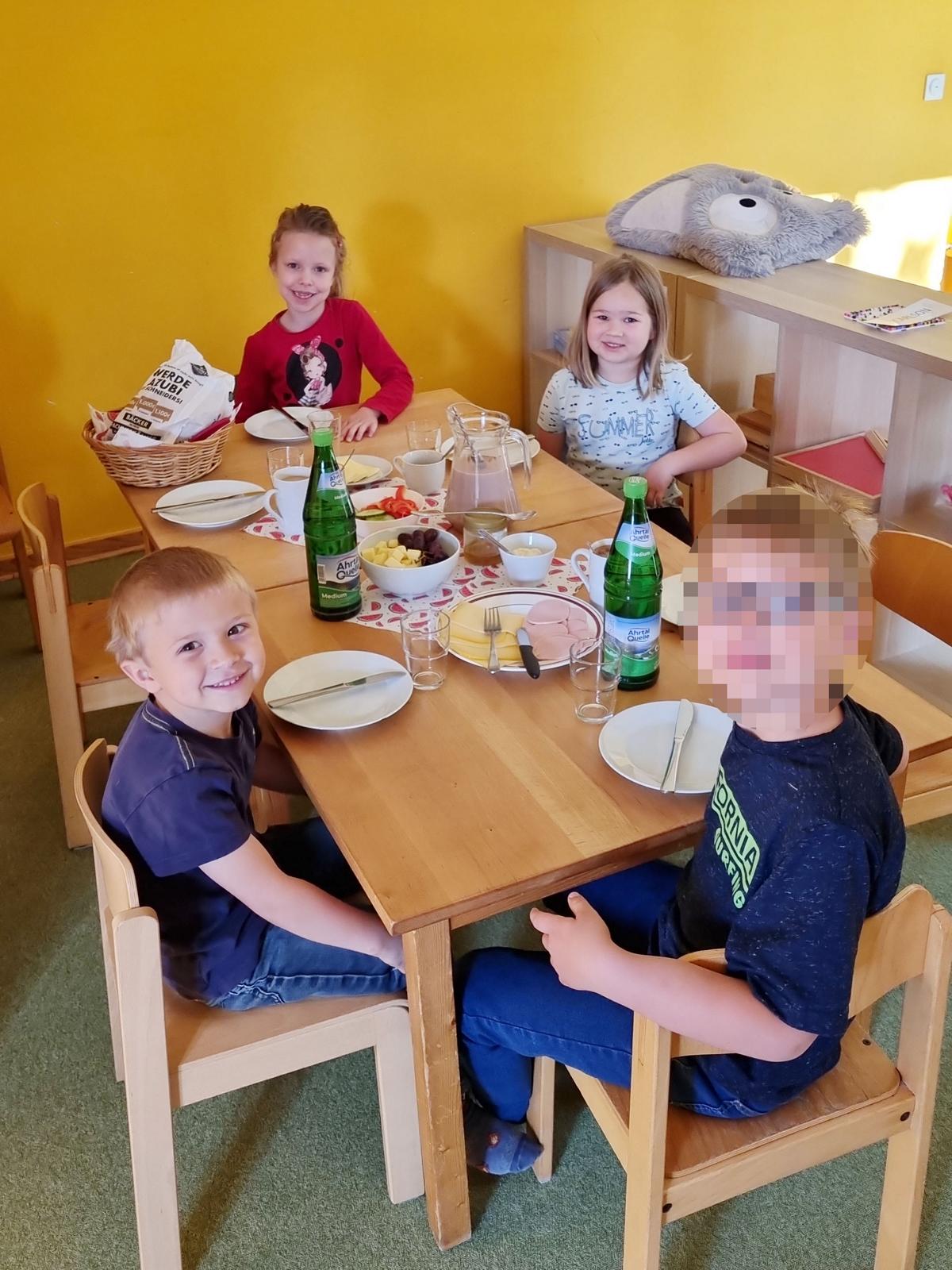 4 Kinder sitzen beim gemeinsamen Frühstück und schauen in die Kamera